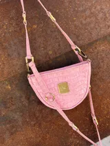 Bandolera de cuero color rosado con textura croco, diseño semicircular, herrajes de bronce y correa regulable y adaptable.