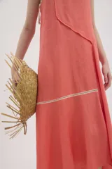 Vestido midi de lino color salmón, de corte amplio y silueta holgada. Presenta diseño con cortes irregulares y detalles de pasamanería en el escote y costuras. Cuenta con breteles dobles tipo cuerda y ruedo asimétrico.