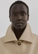 Chaqueta corta de algodón en color beige, con cuello camisero, mangas largas, dos bolsillos con solapa en el frente y cierre de botones.