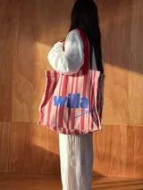 Bolso tipo tote bag de lienzo grueso de algodón con diseño de rayas rojas y blancas, asas de hombro rojas y estampa frontal con la palabra "willa" en color azul.