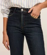 Pantalón de jean de corte slim, color azul oscuro, con trabillas en la cintura, cierre por botón y cremallera, bolsillos y aberturas en los bajos.