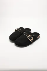 Pantuflas negras de gamuza sintética con interior de corderito, detalle de tira con tachas metálicas doradas y hebilla decorativa, y suela de corcho.