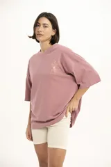 Remera color marrón de corte holgado, con cuello redondo y manga corta. Presenta un pequeño estampado dorado de una flor en el pecho.