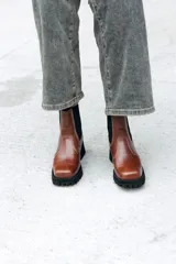 Bota tipo Chelsea de cuero color marrón, con paneles laterales elásticos en color negro y suela track robusta de goma negra.
