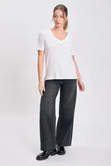 Pantalón de jean negro de corte recto y tiro alto, con detalle de tachas metálicas plateadas a lo largo de las costuras laterales.