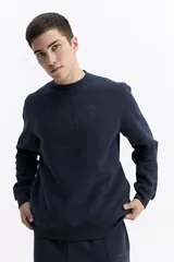 Buzo de cuello redondo en color azul marino, confeccionado en tejido de algodón con mezcla. Presenta una estampa frontal con el nombre de la marca en relieve tonal y puños y ruedo acanalados.