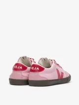Championes Veja modelo Volley, de diseño inspirado en el voleibol de los años 70. Presentan una base de cuero en color rosa, con detalles en rojo en el logo lateral, talón y cordones. Cuentan con refuerzos de gamuza en la puntera y una suela de goma en color marrón oscuro.