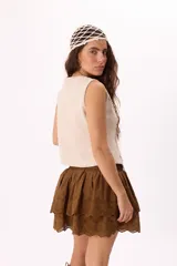 Chaleco color crema con escote en V y cierre frontal con lazos. Presenta detalles de puntilla en el escote y calados en los laterales.