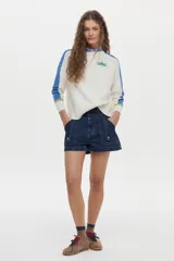 Sweater de punto color blanco con mangas raglán en azul y detalles en verde en los puños, cuello redondo y bordado de libélula en el pecho.