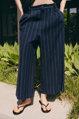 Pantalón de tiro medio confeccionado en mezcla de lino, con diseño de rayas verticales. Presenta cintura con trabillas, bolsillos laterales, pinzas en el delantero y cierre frontal con cremallera y botón.