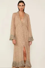 Vestido largo beige estampado con diseño floral, con forro, escote en V con cierre de botones delanteros y mangas largas con puños anchos con volados. Presenta una silueta fluida, detalles plisados y un volante superpuesto en el bajo.