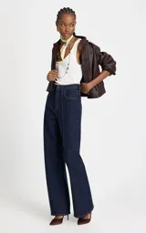 Jean de corte recto y tiro alto, confeccionado en denim azul oscuro. Presenta costuras verticales frontales que estilizan la silueta, cintura estructurada con trabillas, bolsillos funcionales y cierre frontal con botón y cremallera.