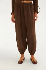 Pantalón babucha marrón de corte amplio y holgado, con cintura alta elastizada y cordón ajustable. Cuenta con puños fruncidos con elástico en los tobillos y está confeccionado en mezcla de viscosa y poliamida con forro de viscosa.