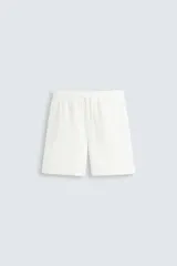 Bermuda de algodón color blanco, de corte regular y largo a la rodilla. Presenta cintura elástica ajustable con cordón, bolsillos laterales y un bolsillo trasero de vivo.