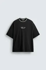 Camiseta de corte boxy fit color negro, con cuello redondo acanalado en contraste blanco y negro. Presenta estampado de texto en relieve en el pecho.