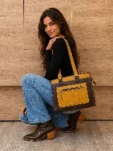 Cartera de cuero marrón de tamaño medio con diseño estructurado, que combina cuero liso y un panel frontal texturizado tipo cocodrilo con bolsillo exterior con cierre. Cuenta con doble asa de hombro y costuras visibles de contraste.