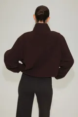 Campera deportiva de sherpa marrón con cuello elevado, cierre frontal y bolsillos laterales.