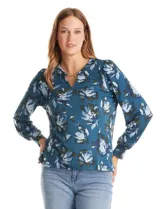 Blusa de seda fría con estampado floral en tonos verdes y azules. Presenta escote en V con un aplique metálico decorativo, mangas largas con puños y corte recto.