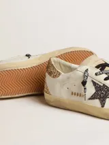 Zapatillas Golden Goose modelo Super-Star en color blanco, con acabado desgastado, la emblemática estrella lateral y detalle en el talón con brillo dorado, además de cordones estampados.