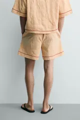 Shorts relaxed fit color beige con textura en relieve tipo jacquard, cintura elástica con cordón ajustable y detalle de bordado en contraste en el bajo.