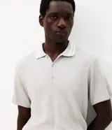 Remera polo marrón de tejido de tricot texturizado, de manga corta, con cuello polo abotonado y detalles de rayas blancas en el cuello.