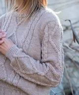 Sweater de punto tejido a mano en lana merino de color gris, con diseño texturado de trenzas y rombo central en el frente y las mangas, y cuello redondo a la base.