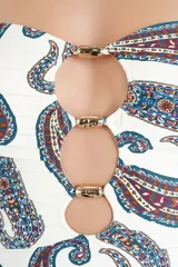 Malla enteriza de color blanco con estampado paisley en tonos azules, marrones y rojos. Presenta diseño bandeau con tirantes finos ajustables, escote con aberturas circulares unidas por argollas metálicas doradas.