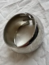 Brazalete plateado rígido con textura martillada y cierre con bisagra.