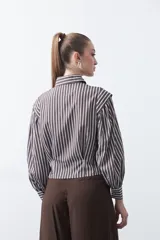 Camisa a rayas azules y blancas de manga larga, con cuello clásico y puños abotonados. Presenta un diseño entallado en la cintura.