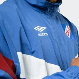 Buzo tipo rompevientos de nylon con medio cierre frontal, cuello alto y puños elásticos. Presenta un diseño en bloques de color azul, blanco y bordó, con el escudo del Club Nacional de Football y el logo de Umbro estampados en el pecho.