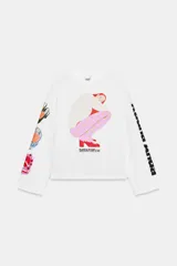 Camiseta blanca de corte oversize con cuello redondo y manga larga. Presenta una estampa gráfica central de una figura femenina, detalles estampados en la manga derecha y texto en la manga izquierda.