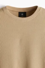 Remera de manga larga en punto waffle color beige, con cuello redondo y ribete acanalado en cuello y puños. Presenta un corte ajustado que realza la silueta.