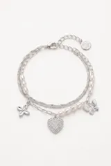Pulsera de doble cadena plateada con perlas cultivadas intercaladas. Presenta tres dijes colgantes: una flor de cuatro pétalos, un corazón pavé con cristales y una mariposa. Incluye cierre de mosquetón y cadena de alargue con medalla grabada.