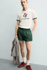 Camiseta de corte relajado confeccionada en piqué de algodón color crudo. Presenta cuello redondo, mangas cortas con ribetes a contraste y estampado frontal con el logo de Italia 90 FIFA World Cup.