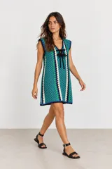 Vestido corto de tejido tipo crochet con diseño de damero en tonos azul y verde, escote en V con cordones negros para ajustar y detalles en blanco y negro.