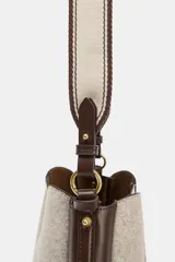 Bolso tipo saca con diseño estructurado, confeccionado en una combinación de tejido de lana en tono beige y laterales de cuero sintético marrón. Presenta costuras decorativas verticales, asa de mano superior y una correa bandolera extraíble con detalle de franjas. Cuenta con cierre mediante botón imantado.
