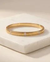 Pulsera tipo esclava rígida de acero con baño de oro, con diseño estriado y detalles de incrustaciones de circonia.