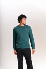 Buzo verde oscuro de cuello redondo, mangas largas con puños elásticos y pequeño estampado ovalado en el pecho.