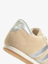 Zapatillas Adidas Taekwondo Lace W color beige con las tres tiras plateadas y refuerzo plateado en el talón.