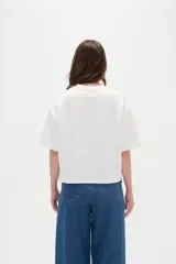 Remera blanca de manga corta, con cuello redondo a la base y diseño holgado.