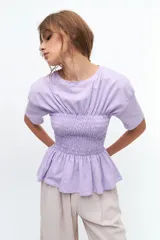 Remera blanca de algodón con cuello redondo, mangas cortas y detalle de fruncido tipo nido de abeja en la zona del busto, creando un efecto peplum.