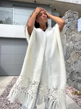 Ruana tejida en punto liso color blanco, con terminación en el ruedo de crochet calado y flecos largos.
