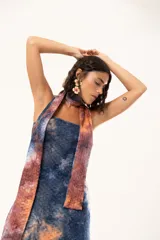 Vestido largo de corte recto y escote strapless, con estampado estilo batik en tonos azul, naranja y bordó. Incluye una bufanda larga integrada al diseño que cae desde el cuello.