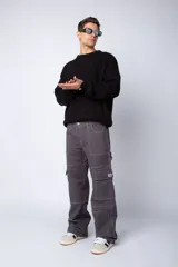 Pantalón tipo carpintero de corte relaxed fit y tiro medio, confeccionado en denim negro con costuras a contracolor en blanco. Presenta múltiples bolsillos cargo laterales, un bolsillo con cierre en la parte inferior y presillas utilitarias.