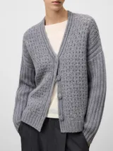 Cardigan gris melange de lana con cuello en pico y cierre frontal de botones. Presenta un diseño de punto calado en el cuerpo y mangas largas con acabado en canalé.
