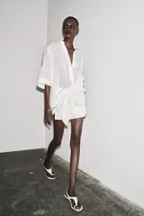 Camisa de color mostaza, con cuello solapa, manga corta y bajo recto. Cierre frontal con botones.