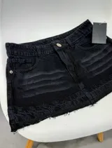 Minifalda de denim negro con efecto desteñido y lavado ácido, tiro medio, cierre frontal con botón metálico y bragueta, bolsillos delanteros y diseño de corte recto con dobladillo deshilachado.
