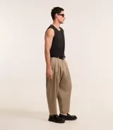 Pantalón de vestir color beige, de corte amplio estilo japonés, con cintura con trabillas, cierre tradicional, pliegues frontales, bolsillos laterales y traseros, y efecto satinado.