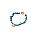 Pulsera elástica con cuentas cúbicas de piedra reconstituida azul y cuentas de nácar. Incluye un dije circular dorado.