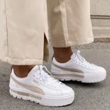 Championes Puma modelo Mayze, de diseño urbano con plataforma alta. Presentan una base blanca con la característica franja lateral de la marca en color negro y detalles en la suela.